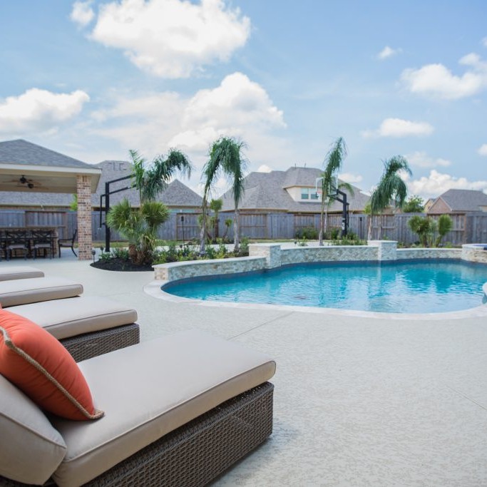 White patio design with in-ground pool and orange accent pillows